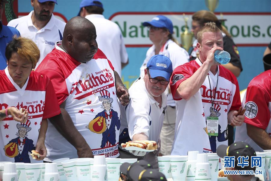 7月4日，在美国纽约康尼岛举行的吃热狗大赛上，工作人员为选手添加热狗。