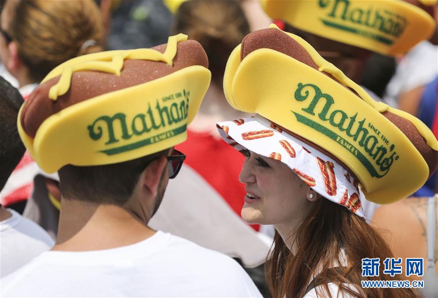7月4日，在美国纽约康尼岛，人们头戴热狗造型帽子观看吃热狗大赛。