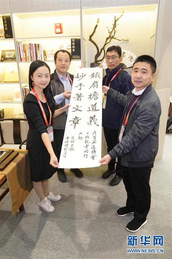 11月8日，在进博会新闻中心，光明日报记者颜维琦（左一）展示她的书法作品。 新华社记者 沈伯韩 摄