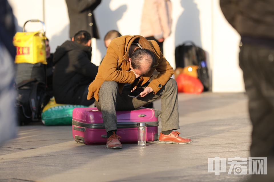 广场上一位旅客低着头看手机。 中宏网记者 富宇 摄