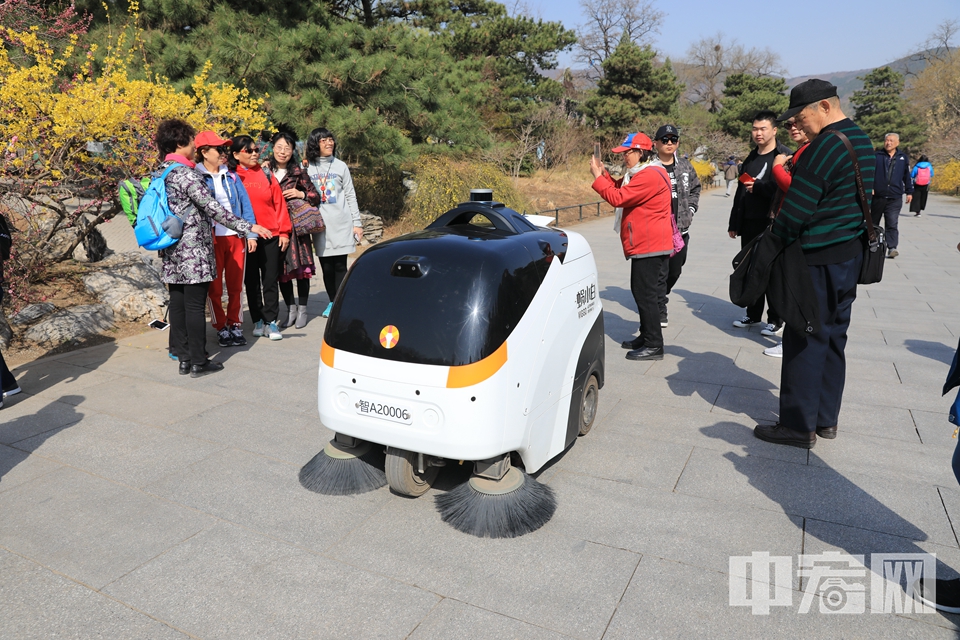 中宏网北京3月26日电（记者 富宇）近日，前往北京植物园踏青赏花的市民会发现新的一景，一辆在园内“巡逻”的无人驾驶清扫车。这辆行驶在北京植物园内的无人驾驶清扫车名为“蜗小白”，它的功能十分强大。它依靠自身摄像头、激光雷达和超声波，远程监控，以及算法和程序的设定，能在靠近游客时执行避让和停靠动作。并自主完成路面清扫、洒水、垃圾收集等工作。图为“蜗小白”经过几名拍照的游客，自动避让。