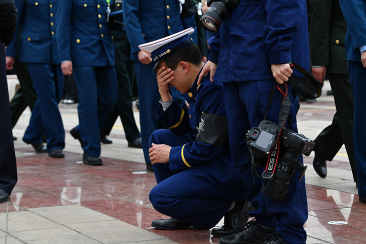 在追悼会现场，一名从木里火场归来的消防员跪地掩面哭泣，久久不愿离去。