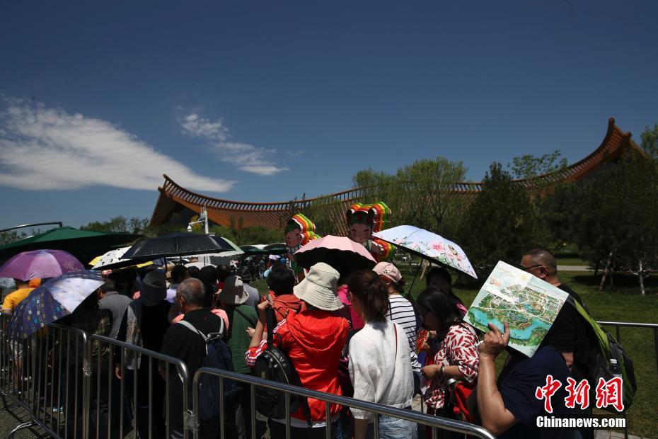 5月22日，游客在北京世园会中国馆门口排队等待，并通过打伞、戴帽子等方式遮阳防晒。当日，京城启动“高烤”模式。北京市气象台于日前发布高温黄色预警，预计22日至25日，北京大部地区日最高气温将达35℃以上，其中23日的局地最高气温可达37℃以上。中新社记者 盛佳鹏 摄