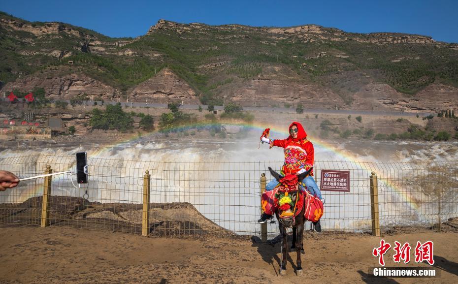 图为在瀑布彩虹前，游客骑上毛驴，穿上陕北民俗服饰留念。兰华 摄 图片来源：中新网