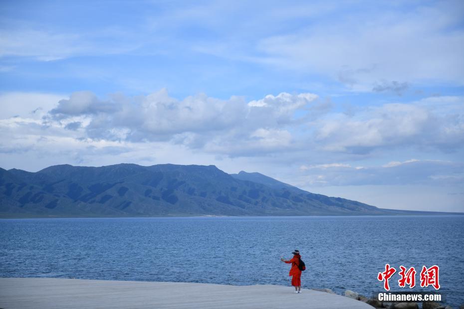 进入六月中旬，新疆赛里木湖景区内，湛蓝的湖水与天一色，同远处山峰相映成画，景色迷人，吸引游客来此游玩、避暑。赛里木湖位于天山山脉，湖面海拔两千多米，水域面积450多平方公里，是新疆海拔最高、面积最大的高山湖泊。图为6月15日，游客在景区内拍照留念。中新社记者 张兴龙 摄