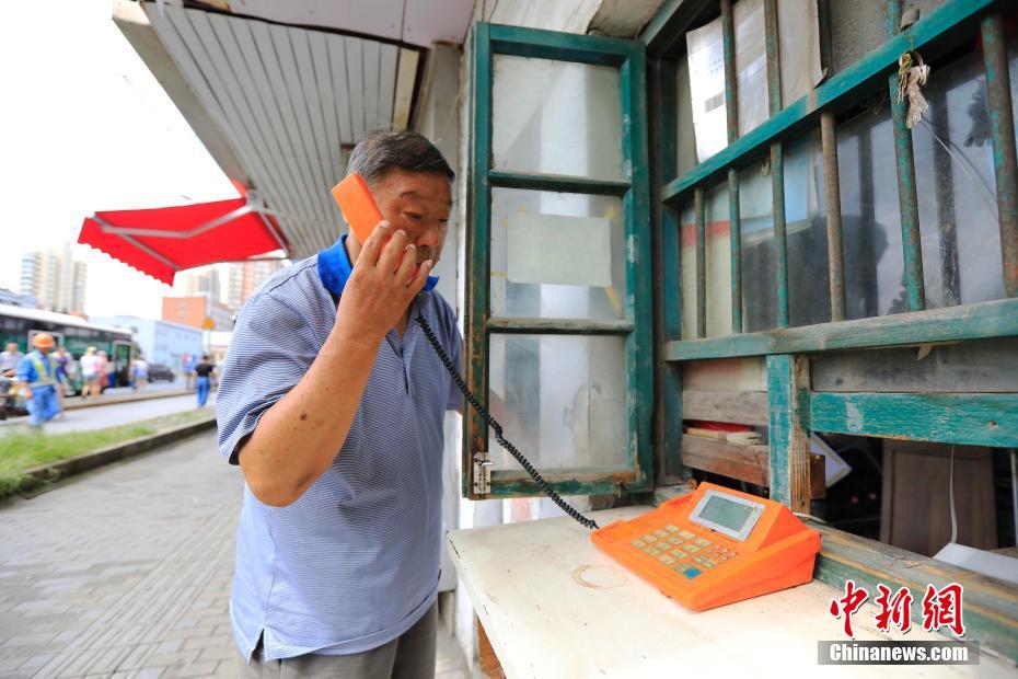 8月5日，在上海市浦东新区浦东大道2511弄门口，有一处不到3平方米的公用电话亭——一块白色小搁板从木窗户里伸出，上面是一台橙色的电话机。这是上海最后的传呼公用电话亭，88岁的吕树生在这里一坐就是25年。如今他上午8点开门，下午4点就关门了。据上海电信公司工作人员介绍，在住宅电话的普及和移动通信的发展之下，上海的传呼电话自21世纪以来开始渐渐退出市民的生活。图为88岁的吕树生在测试电话设备。殷立勤 摄