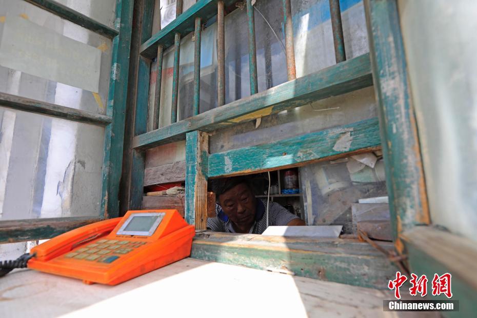 8月5日，在上海市浦东新区浦东大道2511弄门口，有一处不到3平方米的公用电话亭——一块白色小搁板从木窗户里伸出，上面是一台橙色的电话机。这是上海最后的传呼公用电话亭，88岁的吕树生在这里一坐就是25年。如今他上午8点开门，下午4点就关门了。据上海电信公司工作人员介绍，在住宅电话的普及和移动通信的发展之下，上海的传呼电话自21世纪以来开始渐渐退出市民的生活。图为88岁的吕树生每天在不到3平方的传呼电话亭里生活着。殷立勤 摄