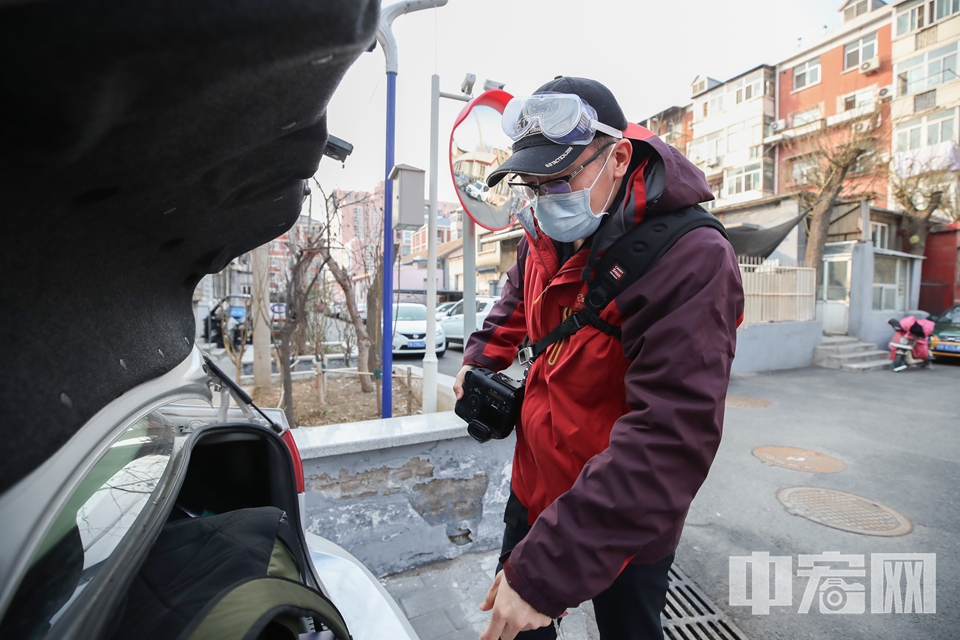 2月25日，身为“西城区注册平安志愿者”的陈硕走进西城区汽南社区，这天他有两个任务，一是他要站好志愿者这班岗，另一个是他还要继续完成已经计划好的采访。因此，背着相机的他，在众多志愿者中显得格外与众不同。图为陈硕从车上拿出摄影器材，疫情期间，他的装备除了摄影器材，还多了口罩、护目镜和酒精。 中宏网记者 富宇 摄