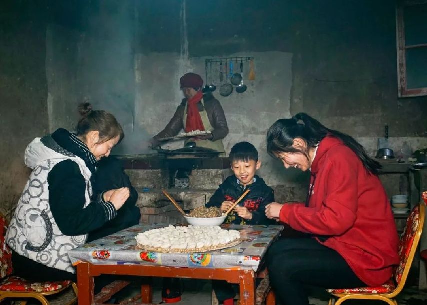 在城里工作的孩子们回到农村老家过年,一家在厨房里边包边煮饺子,其乐