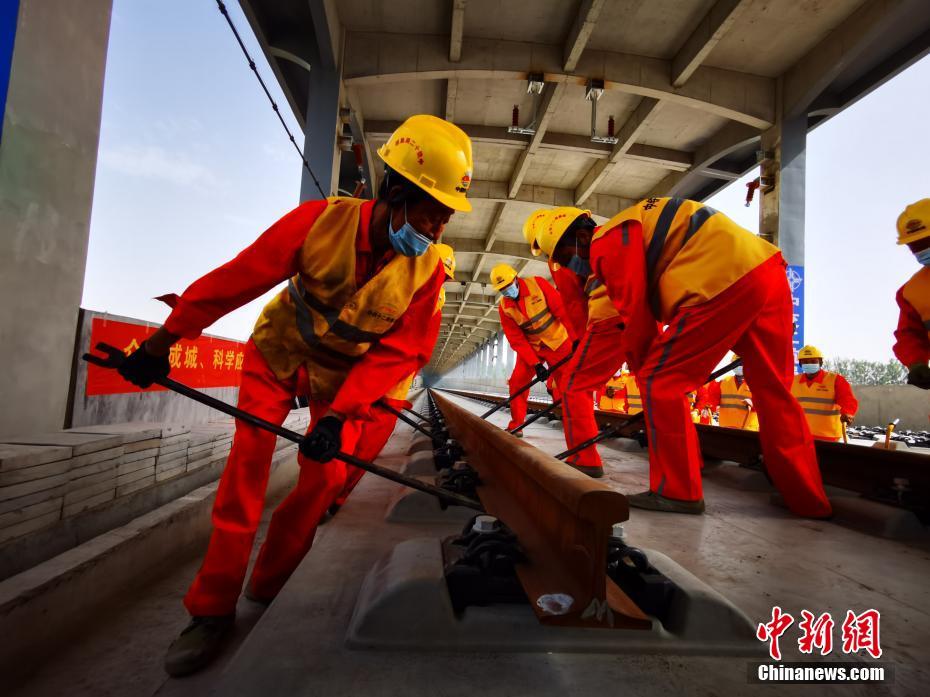 6月3日，在北京至雄安城际铁路（河北段）铺轨施工现场，一组500米长钢轨平稳落在无砟道床上，标志着京雄城际铁路（河北段）建设进入铺轨阶段。京雄城际铁路分两段建设运营，其中大兴机场段设计时速250公里，已于2019年9月开通运营；大兴机场至雄安段设计时速350公里，预计2020年底开通运营。图为工人在北京至雄安城际铁路（河北段）铺轨施工现场进行铺轨作业。 孙丽萍 摄