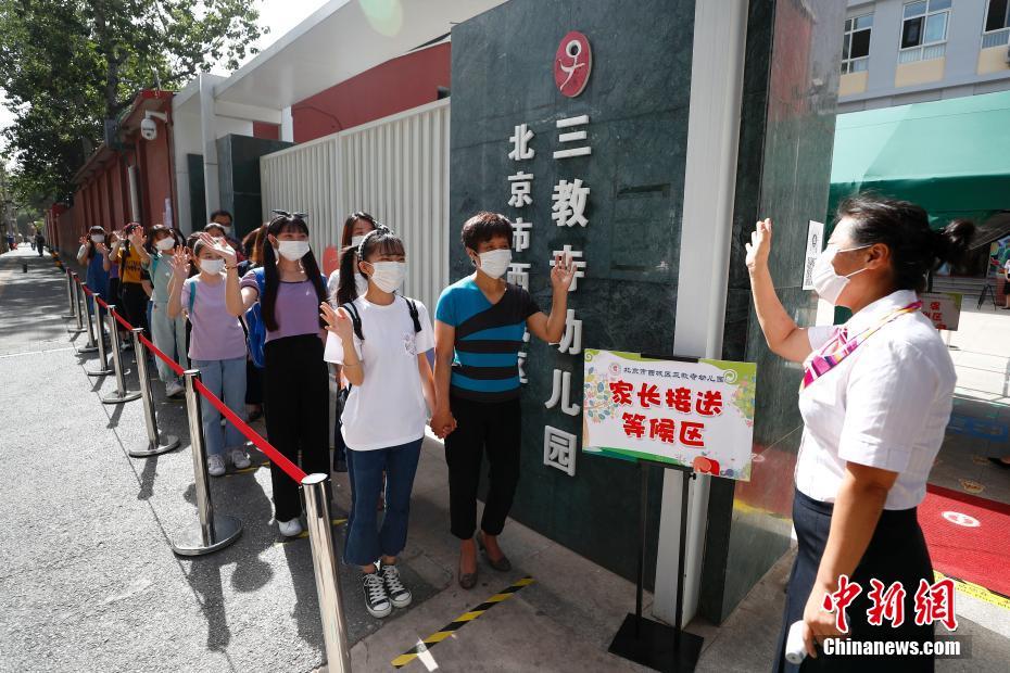 6月3日，北京市西城区三教寺幼儿园开展返园应急演练，对幼儿们返园后可能出现的一系列场景进行全方位“彩排”，通过大、中、小班错峰报到，每日测体温和日常体检耳鼻口手、室内外间隔一米活动等多项措施确保幼儿安全返园。6月8日，北京市具备开园条件的幼儿园可陆续开园。图为老师在校门口演练欢迎“小朋友”返园。 中新社记者 富田 摄