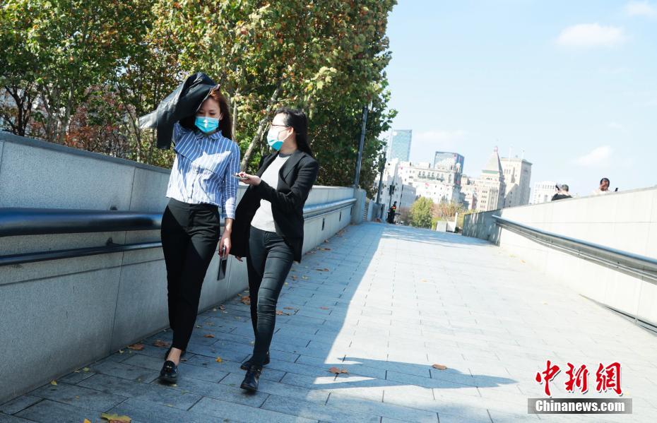 11月18日，上海外滩，行人用衣服遮挡炙热的阳光。当日，上海的温度不断升高，截至14时，徐家汇站的气温已升至27.2℃，刷新了本世纪11月中旬同期最高气温纪录。之前纪录是2002年11月11日和2019年11月17日，日最高气温为24.2℃。 中新社记者 汤彦俊 摄