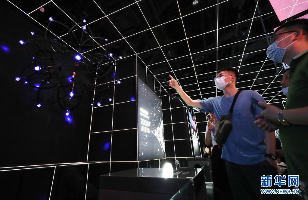7月18日，参观者在“宇宙”展区内一个展示宇宙膨胀理论的模型旁交流讨论。