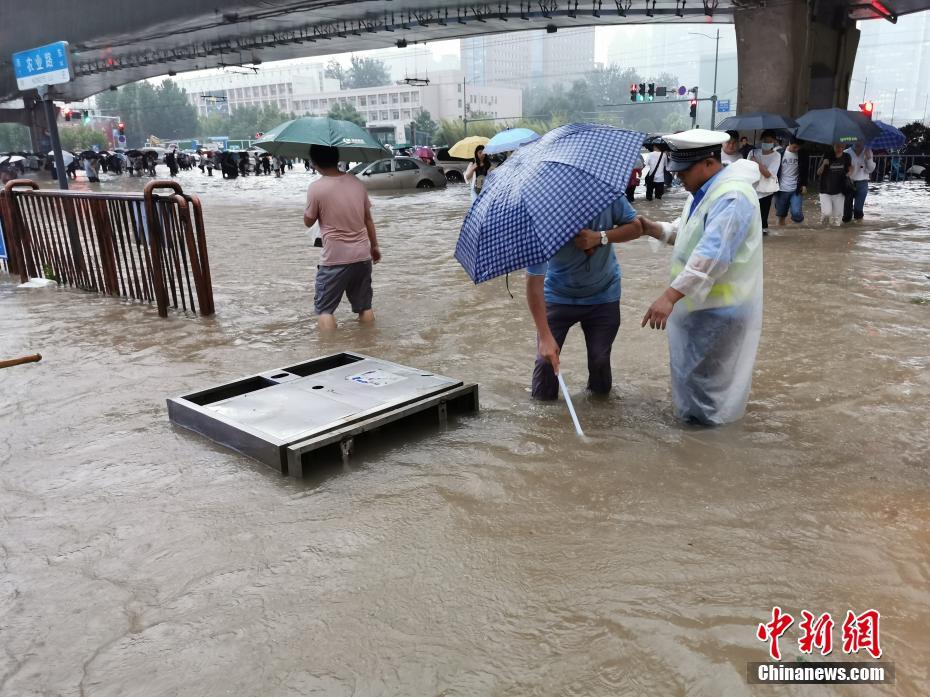 7月20日，持续强降雨导致部分街道积水严重，救援人员冒雨疏通下水口。中新社记者 韩章云 摄