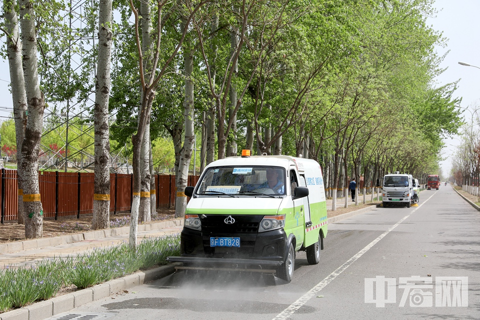 北京市园林绿化局工人对路面上的杨絮进行喷水，抑制飞絮二次飘飞。