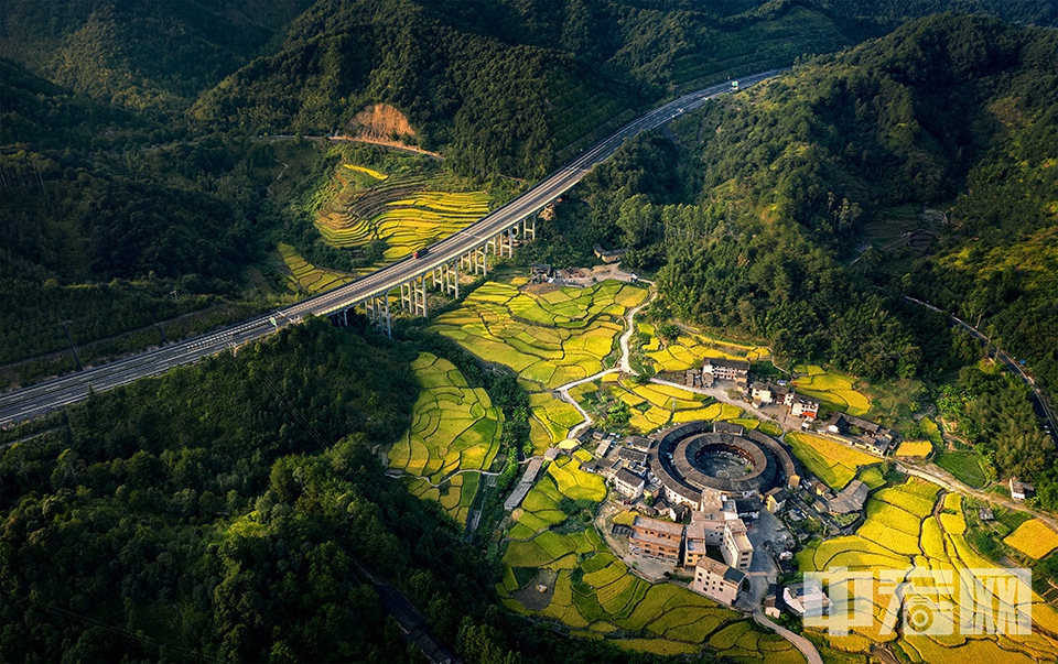 相機(jī)組優(yōu)秀獎(jiǎng)《金秋土樓致富路》作者 張煒    
拍攝于福建省龍巖市永定區(qū)。金秋時(shí)節(jié)，永定區(qū)的莆永高速公路猶如一條致富路，通向了土樓家園。高速路兩旁秋色如畫，美不勝收。莆永高速至建成通車，進(jìn)一步促進(jìn)了海峽西岸經(jīng)濟(jì)區(qū)和珠江三角洲之間的經(jīng)濟(jì)協(xié)作，促進(jìn)了閩西革命老區(qū)經(jīng)濟(jì)發(fā)展及福建土樓旅游文化的發(fā)展。